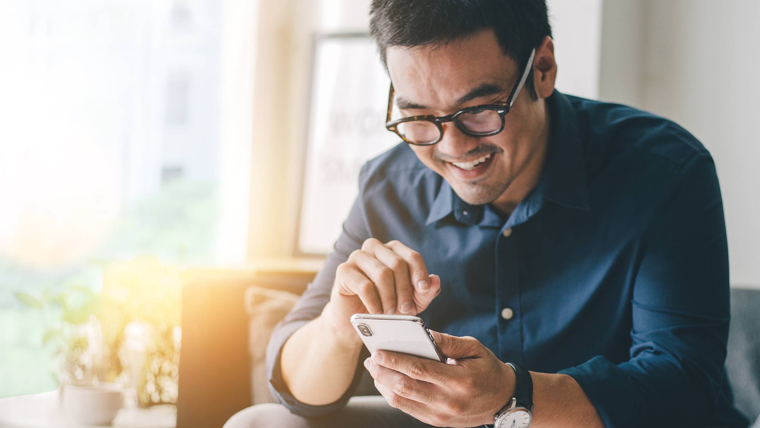 happy man in shirt using phone sitting on sofa